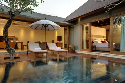 a swimming pool with two chairs and an umbrella at KoenoKoeni Villa in Seminyak