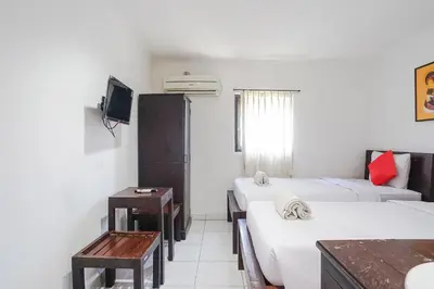 a room with three beds and a tv and a table at Gana Inn Legian in Legian