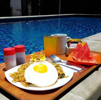 a breakfast plate of eggs and fruit next to a swimming pool at Sari Stay in Jimbaran