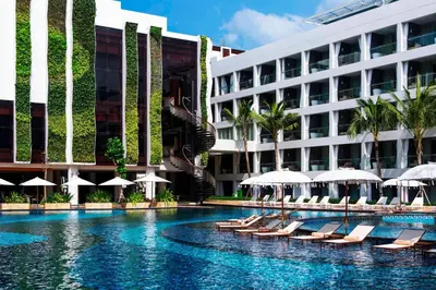 a swimming pool with chairs and umbrellas in front of a building at The Stones Hotel - Legian Bali in Kuta
