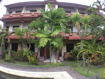 a building with palm trees in front of it at Mangga Bali Inn in Legian