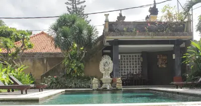 a swimming pool in front of a house with a fountain at Mangga Bali Inn in Legian