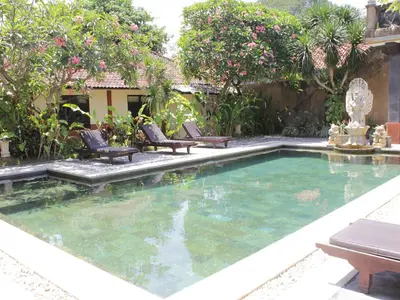 a swimming pool in a yard with chairs and trees at Mangga Bali Inn in Legian