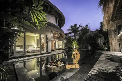 a woman sitting on the edge of a pool next to a villa at Luxury Villas Merci Resort 3BR Seminyak #1 in Seminyak