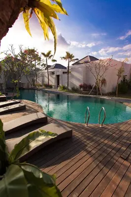 a large swimming pool with a wooden deck next to a house at Daluman Villas in Seminyak