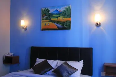a bedroom with a blue wall with a painting above a bed at Asher Bali Transit in Kuta