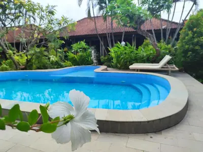 a swimming pool in front of a house with a white flower at Adus Beach Inn in Legian