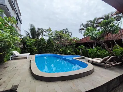 a swimming pool on a patio with chairs and a building at Adus Beach Inn in Legian