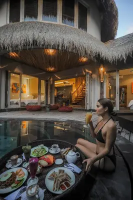 a woman sitting next to a table of food next to a pool at Luxury Villas Merci Resort 3BR Seminyak #2 in Kuta