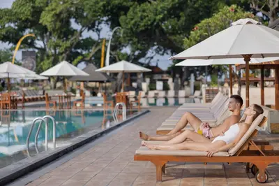 a man and woman sitting on a bench next to a pool at The Jayakarta Bali Beach Resort in Legian