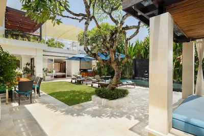 an outdoor patio with a tree and a house at Villa Camellia by Nakula in Jimbaran