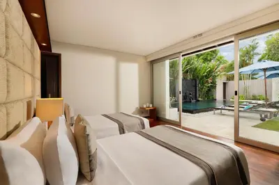 a bedroom with two beds and a patio with a pool at Villa Camellia by Nakula in Jimbaran