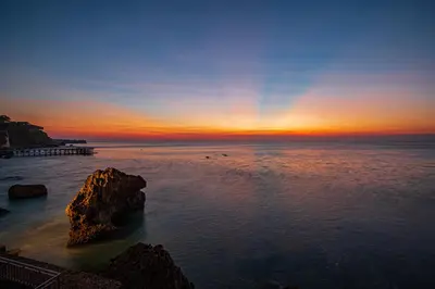 a sunset over the ocean with a rock in the water at Villa Deh Simba at Ayana With Private Pool in Jimbaran