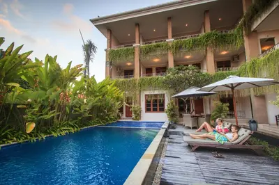 a family sitting on benches by a swimming pool in front of a house at Pondok Anyar Hotel in Kuta