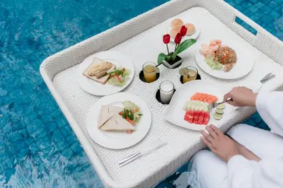 a table with plates of food next to a swimming pool at Amaroossa Suite Bali in Nusa Dua