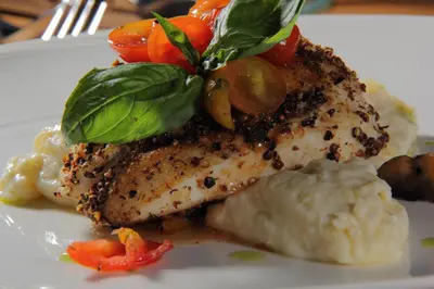 a white plate with a piece of fish with vegetables on it at Amaroossa Suite Bali in Nusa Dua