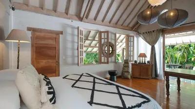 a bedroom with a white bed and a table and windows at Villa Koyama by Villa Finder in Seminyak