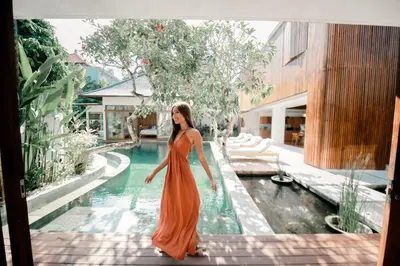 a woman in an orange dress standing next to a swimming pool at Luxury Villa Seminyak near beach and Potato Head in Seminyak