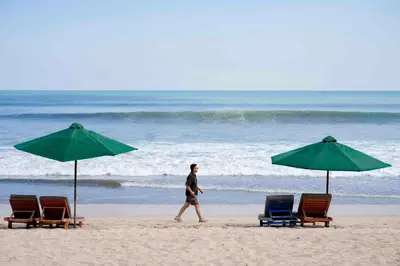 a man walking on the beach with chairs and umbrellas at Solaris Hotel Kuta in Kuta