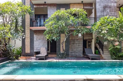 a swimming pool in front of a building with trees at Eddys Cottages & Villa in Legian