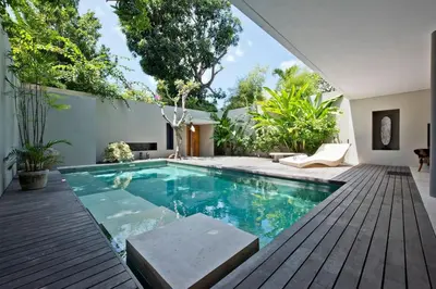 a swimming pool in a backyard with a deck and a house at VILLA OLYMPIA in Seminyak