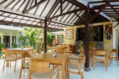 a dining room with tables and chairs under a wooden pergola at Puri Panca Jaya Hotel in Seminyak