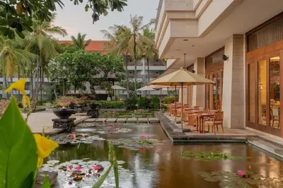 a courtyard with a pond with flowers and tables and chairs at Conrad Bali in Nusa Dua