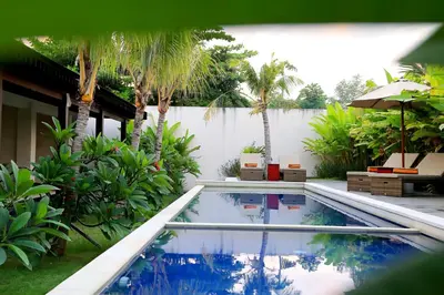 a swimming pool in a yard with palm trees at Kaniya bali in Nusa Dua