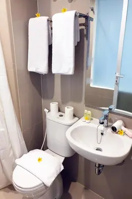 a bathroom with a toilet and a sink and towels at The Rooms Apartment Bali by ARM Hospitality in Denpasar