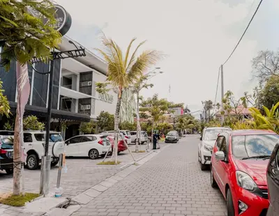 a city street with parked cars and palm trees at The Rooms Apartment Bali by ARM Hospitality in Denpasar
