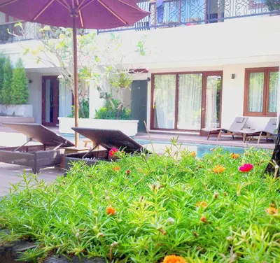 a patio with chairs and an umbrella and flowers at Seminyak Lagoon All Suites Hotel in Seminyak