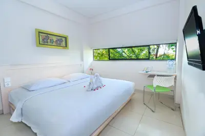 a white bedroom with a bed and a desk at J Hotel Kuta in Kuta