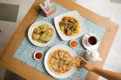 a table with plates of food and a person eating a slice of pizza at The Nyaman Hotel Bali in Kuta