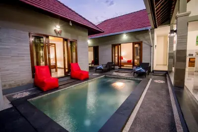 a swimming pool in the backyard of a house with red chairs at Taman Bali Villas Dewi Sri in Legian