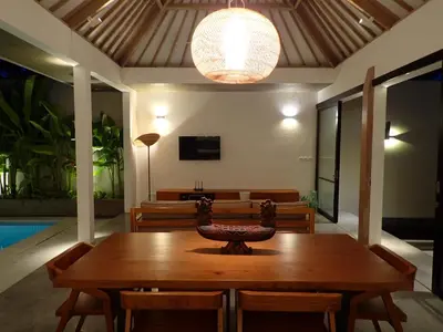 a dining room with a wooden table and a chandelier at Villa Hujan in Seminyak