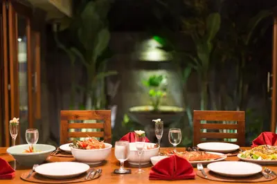 a wooden table with plates of food and wine glasses at Villa Dewata One in Seminyak