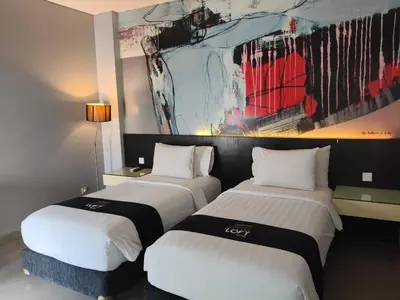 two beds in a hotel room with a painting on the wall at Loft Legian Hotel Bali in Legian