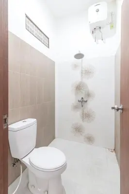 a white bathroom with a toilet and a shower at Kak Garden Inn in Kuta