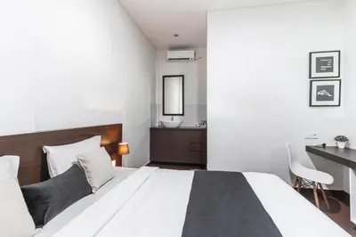a bedroom with a large white bed and a desk at Kak Garden Inn in Kuta