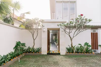 a white house with a door and trees at Kubu Benoa Guest House in Nusa Dua