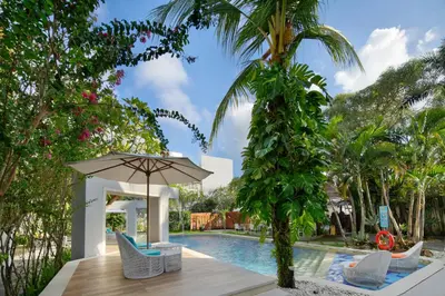 a pool with chairs and an umbrella next to a palm tree at 18 Suite Villa Kuta in Kuta