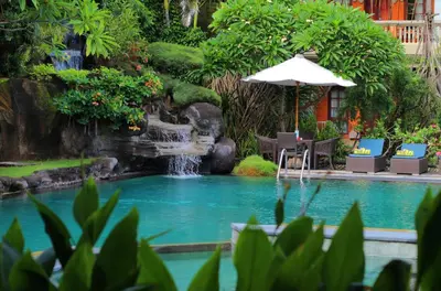 a swimming pool with a waterfall and an umbrella at Adi Dharma Hotel Legian in Legian