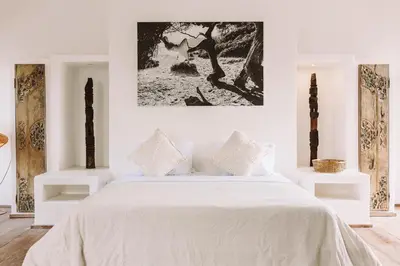 a white bedroom with a white bed and a painting on the wall at La Payesa in Canggu