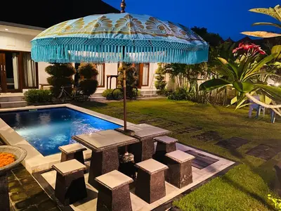an umbrella over a table and stools next to a pool at Villa Pintu Biru in Seminyak