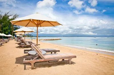 a beach with chairs and an umbrella and the ocean at Capital O 2166 Elitya Stay in Sanur