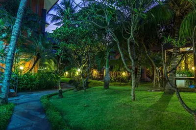 a garden at night with palm trees and a pathway at Bakung Beach Resort in Kuta