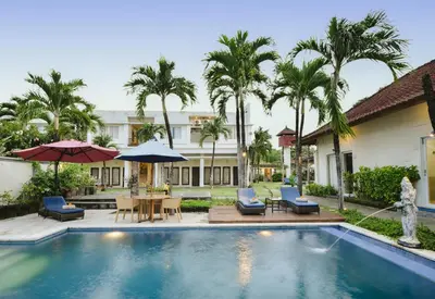 a pool with chairs and umbrellas next to a building at Bali Breezz Hotel in Jimbaran