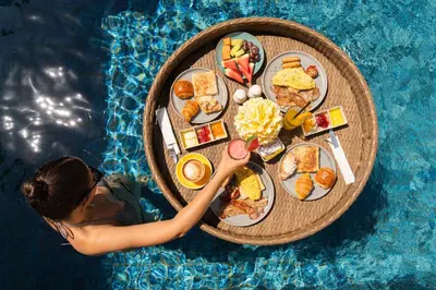 a woman in a swimming pool with a tray of food at Royal Suites at The Bandha in Legian