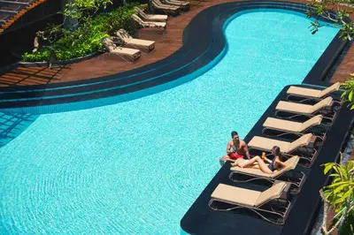 two people sitting on lounge chairs next to a swimming pool at Fairfield by Marriott Bali Kuta Sunset Road in Kuta