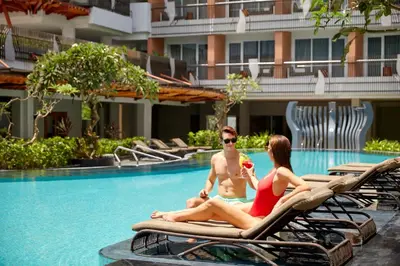a man and woman sitting on lounge chairs by a swimming pool at Fairfield by Marriott Bali Kuta Sunset Road in Kuta